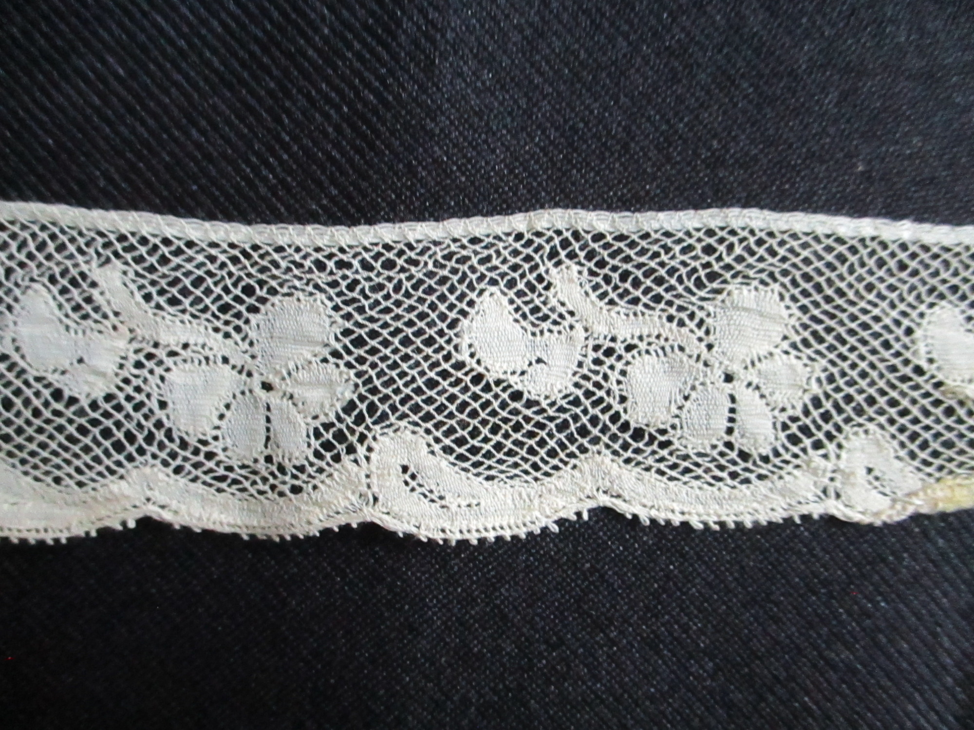 Length of folded silk lace trim.: Design detail on folded cream silk lace trim.
