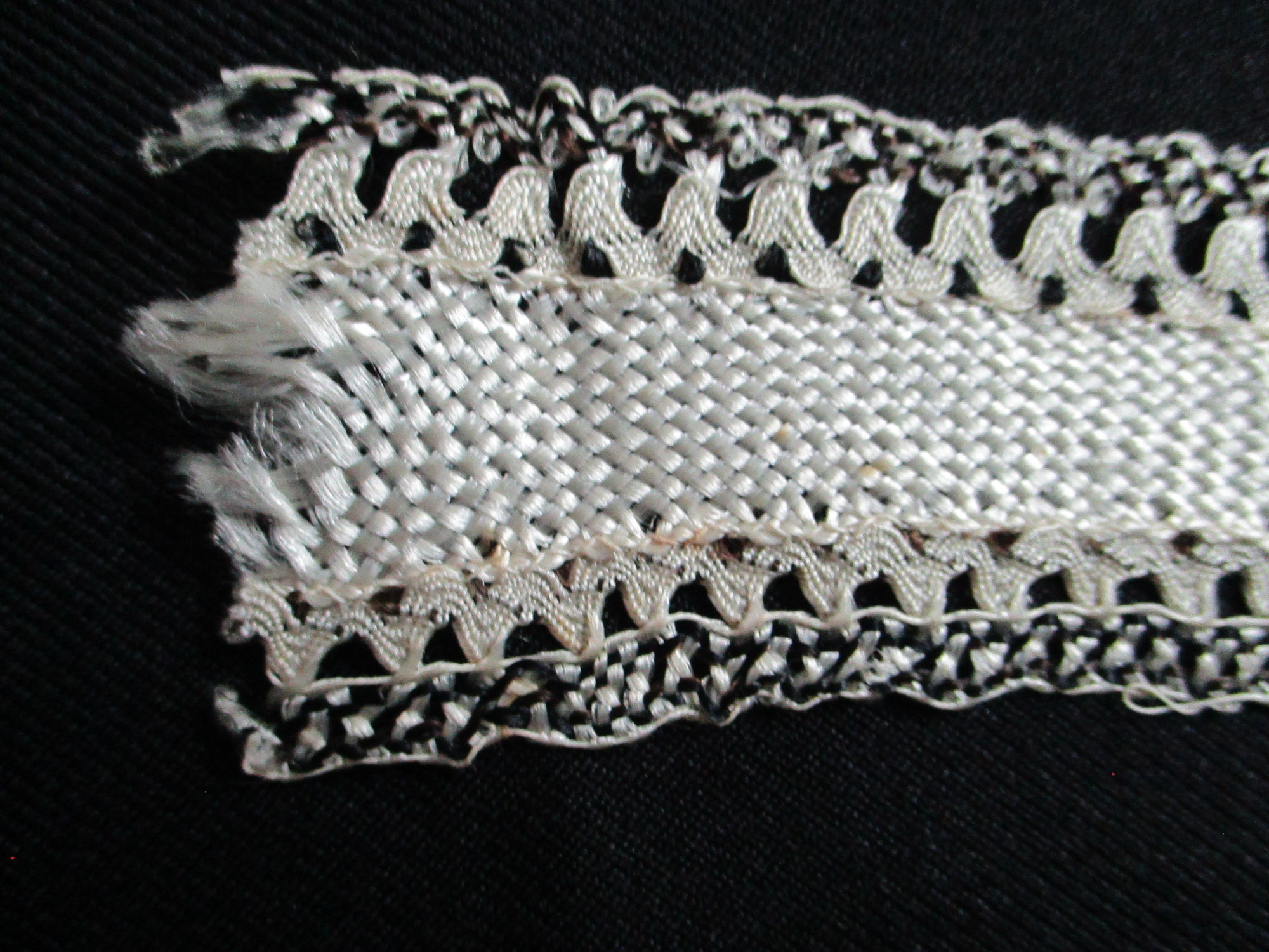 Length of silk ribbon/trim.: Detail of cream and black silk ribbon on black background. (iii0