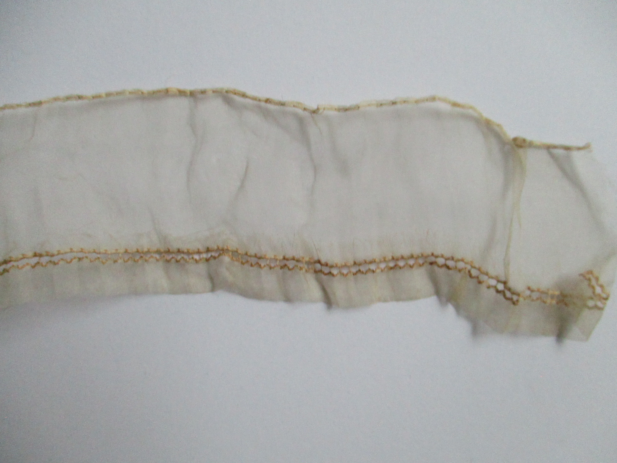 Piece of cream silk edging/trim.: End detail of cream silk ribbon/edging.