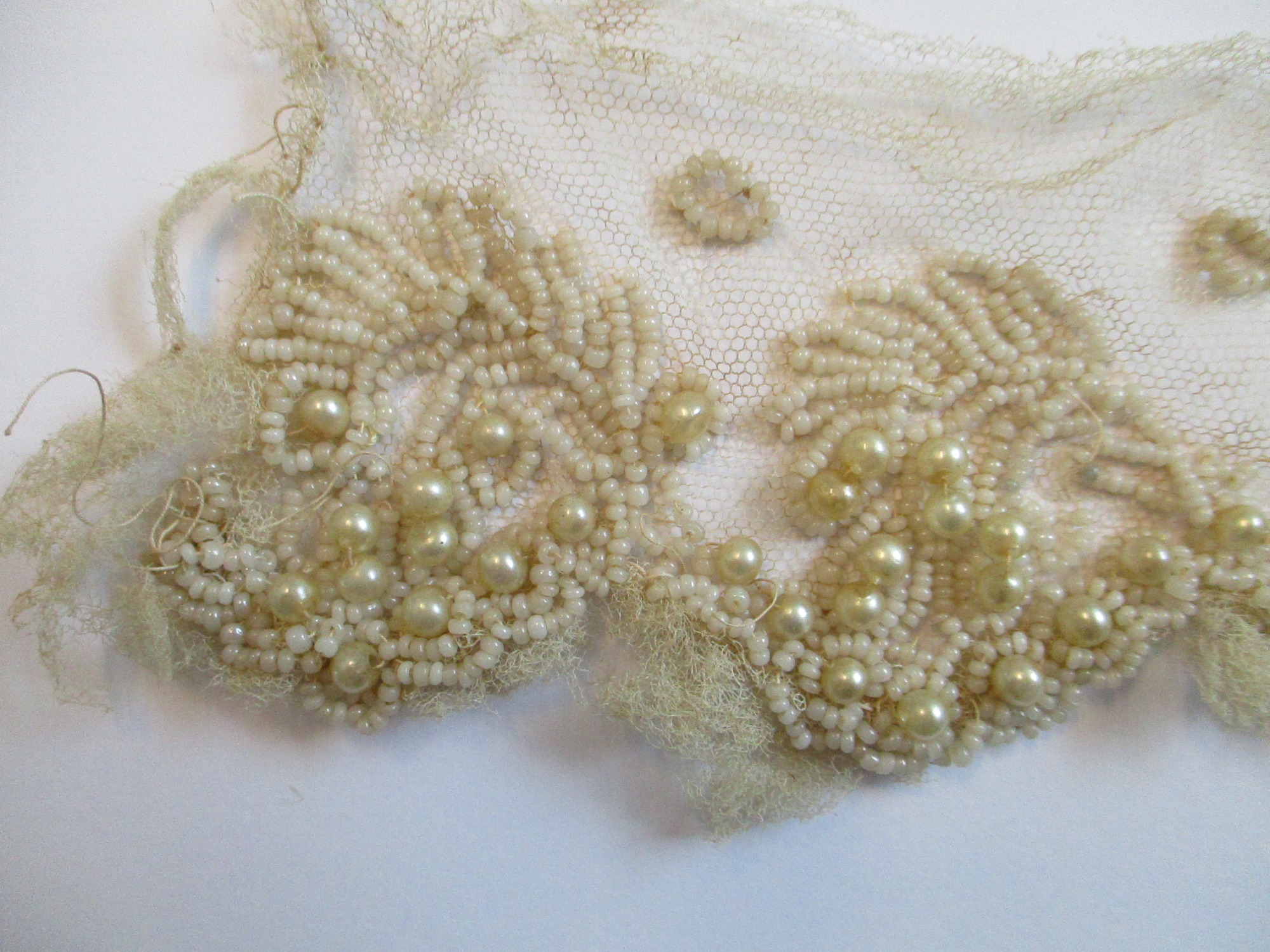 Strips of heavily beaded cream netting: Beading detail on cream netting. (i)