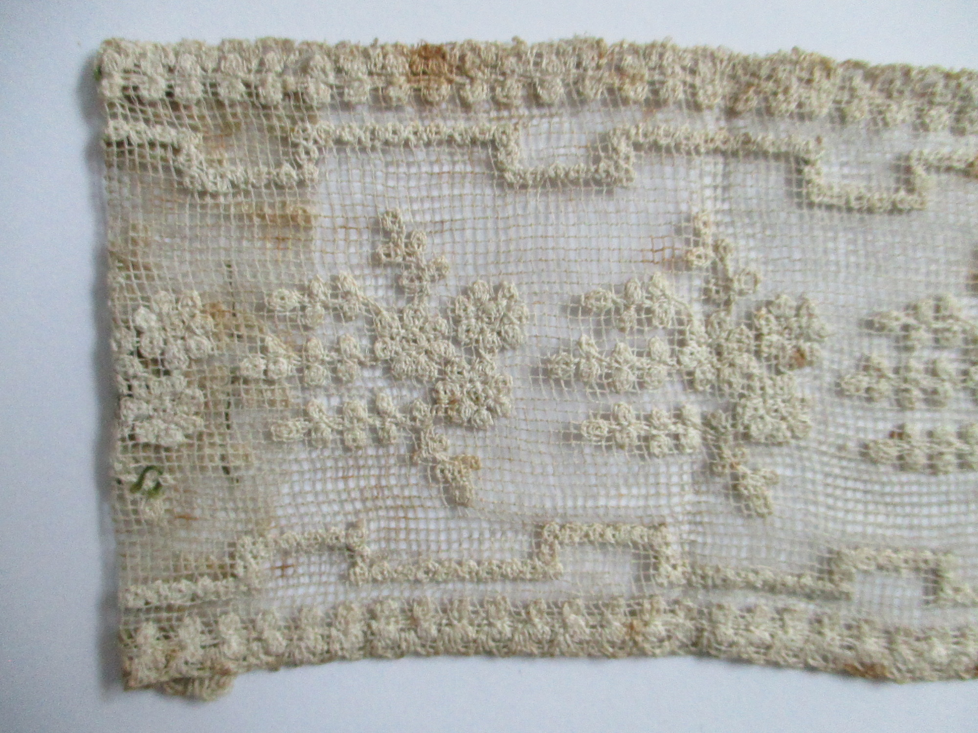 Two pieces of decorated cream netting.: Folded end of cream lace ribbon. (i)