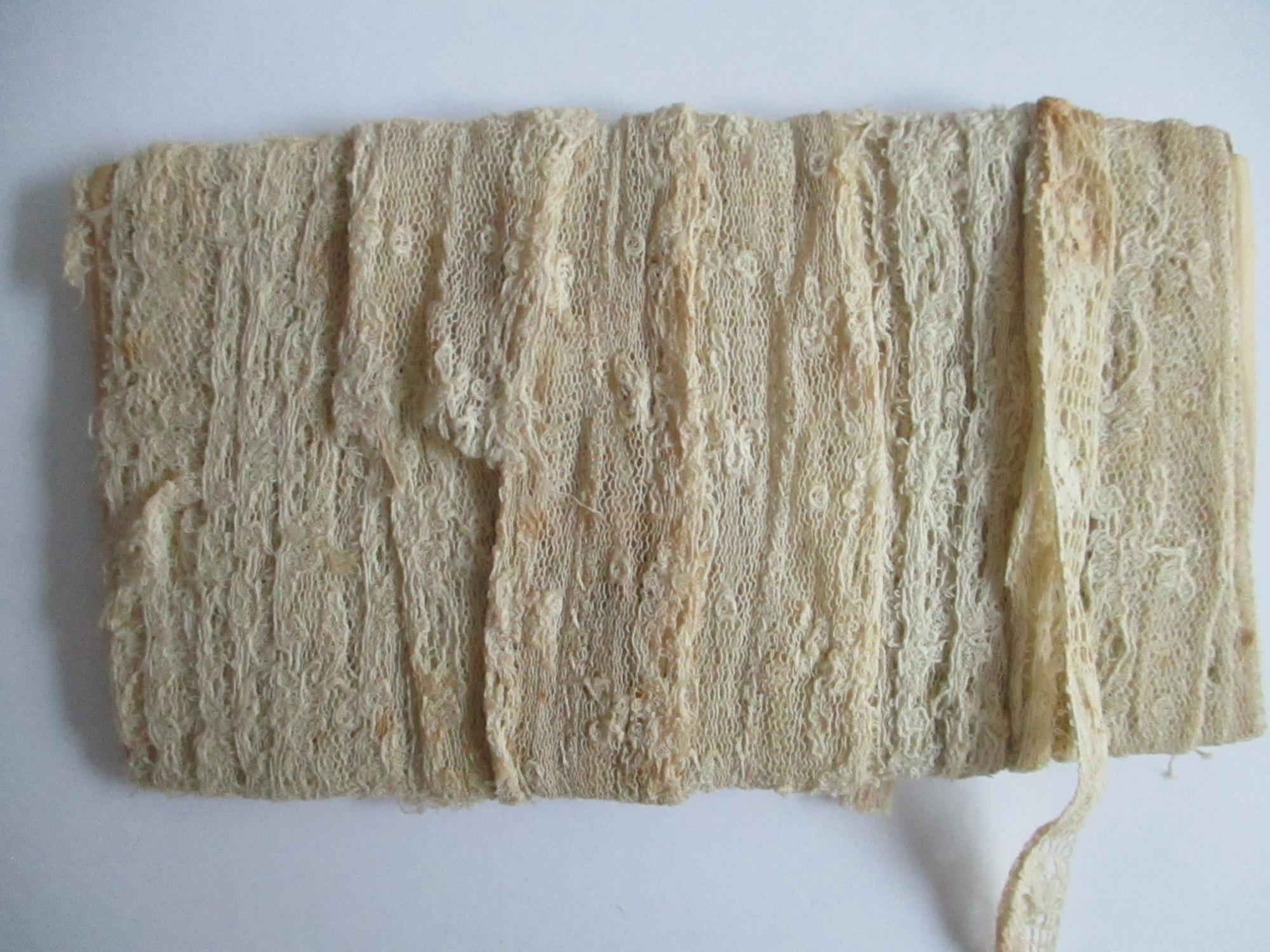 Unused length of lace trim/ribbon wound round paper.: Length of unused cream lace ribbon wound round paper.(i)