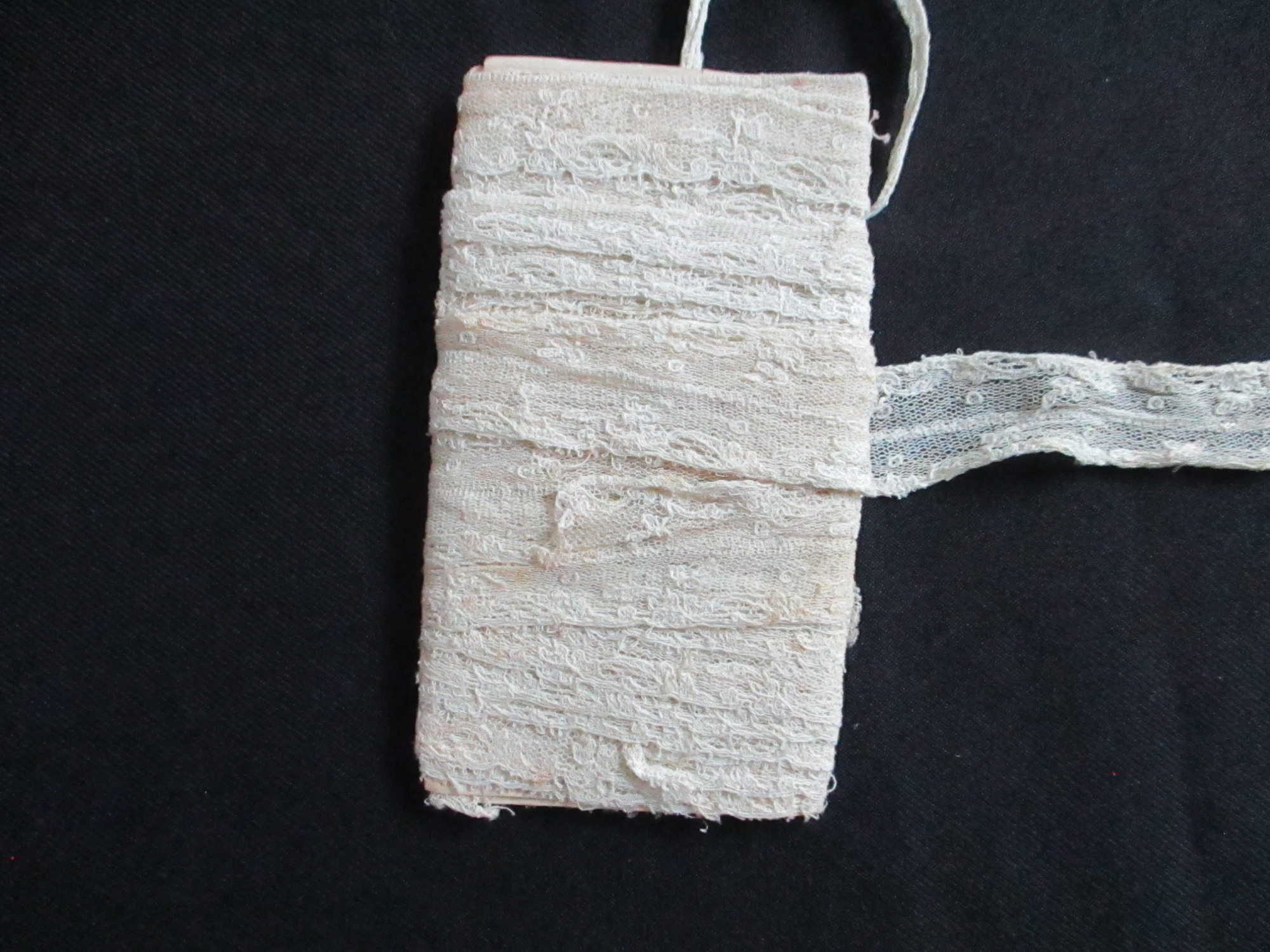 Unused length of lace trim/ribbon wound round paper.: Length of unused cream lace ribbon wound round paper.(iii)